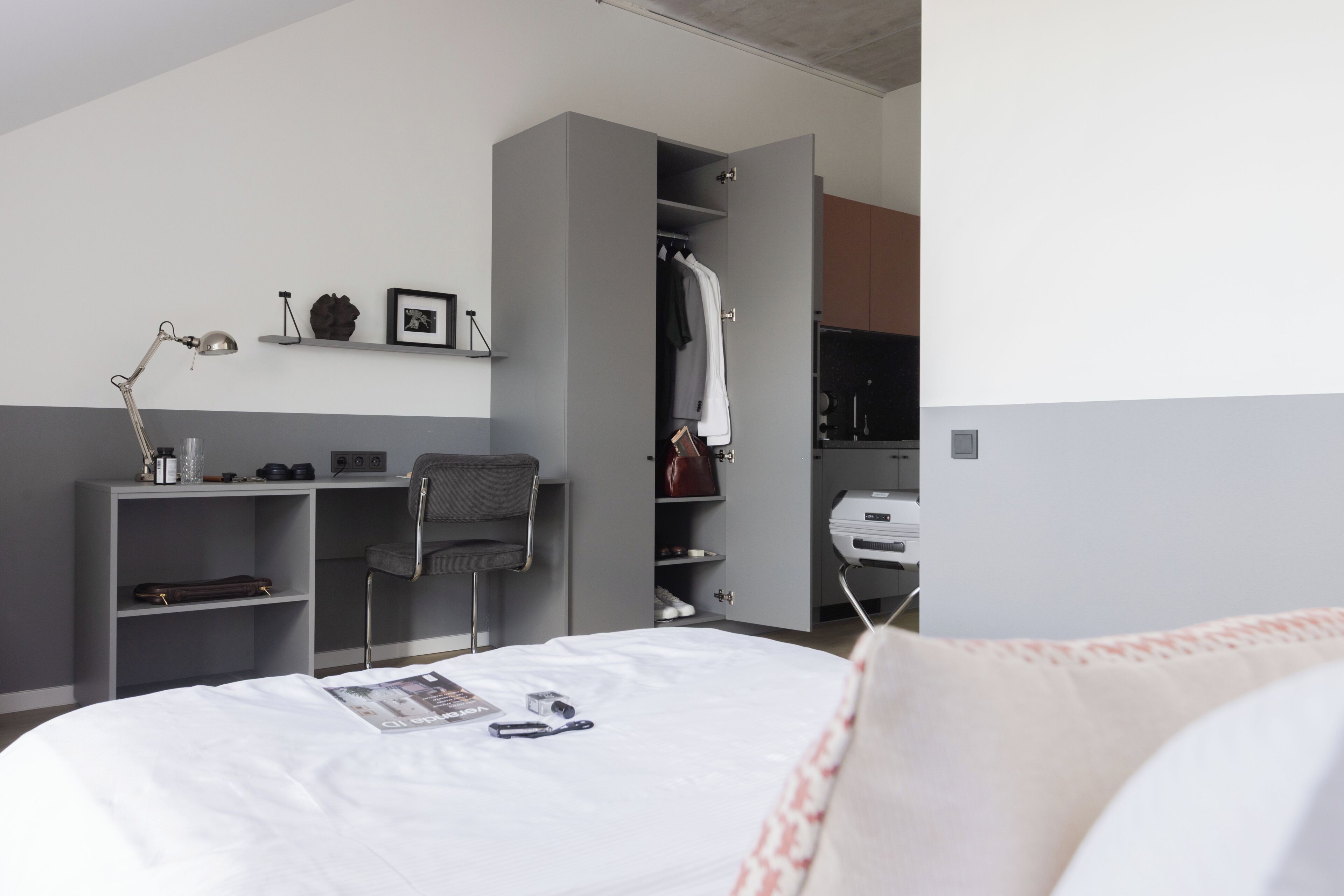 A bedroom with a bed, a desk, a chair, a wardrobe, and a desk lamp.