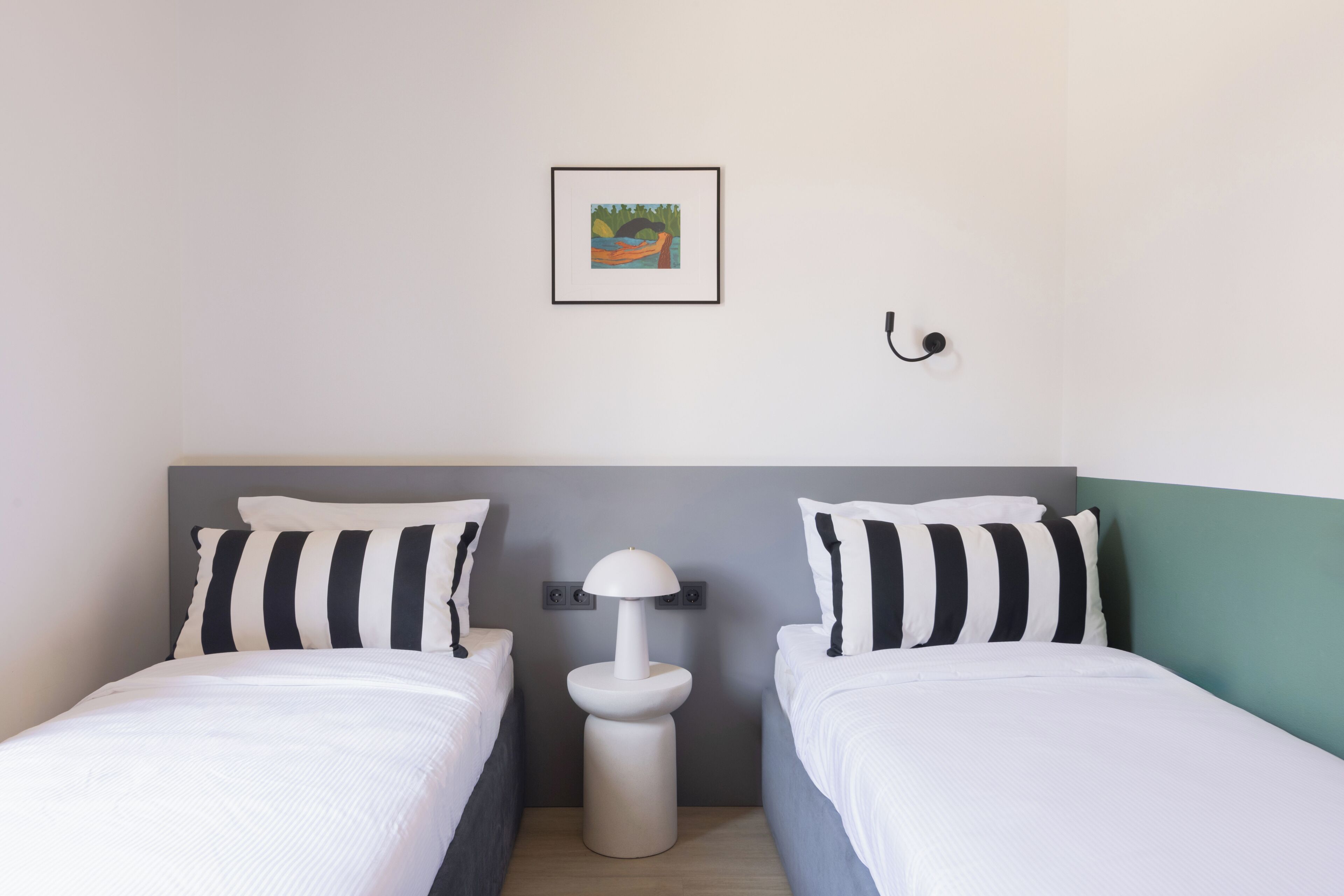 Une chambre double avec deux lits, une table de chevet, une lampe et un tableau encadré au mur.