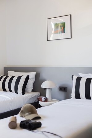 Ein Hotelzimmer mit einem Bett, einem Nachttisch, einer Lampe, einer Kamera und einer Mütze.