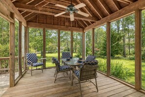 A covered patio with a wooden deck, a table with chairs, and a ceiling fan. - Game Room, Cozy & Mins to Beaches! (Eastham)