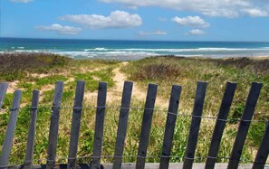 A wooden fence with barbed wire, leading to a beach with ocean waves and a clear sky. - Game Room, Cozy & Mins to Beaches! (Eastham)
