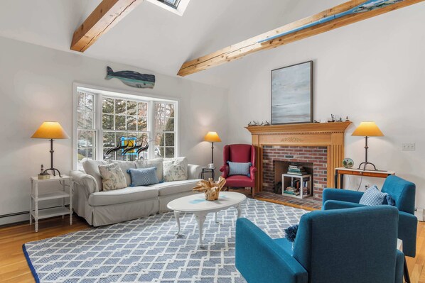 A cozy living room with a fireplace, a sofa, a red armchair, and a blue armchair. - Game Room, Cozy & Mins to Beaches! (Eastham)