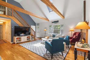 Ein geräumiges Wohnzimmer mit einer Holztreppe, einem Flachbildfernseher, einer Couch, einem roten Sessel und einem Kamin.