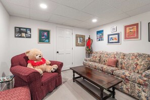 Ein Zimmer mit einem großen Teddybären auf einem roten Sessel, einer floralen Couch, einem hölzernen Couchtisch und verschiedenen gerahmten Kunstwerken an den Wänden.