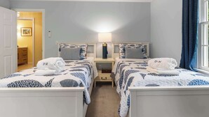 A twin room with two beds, a bedside table with a lamp, a wall-mounted phone, and a window with curtains. - Game Room, Cozy & Mins to Beaches! (Eastham)