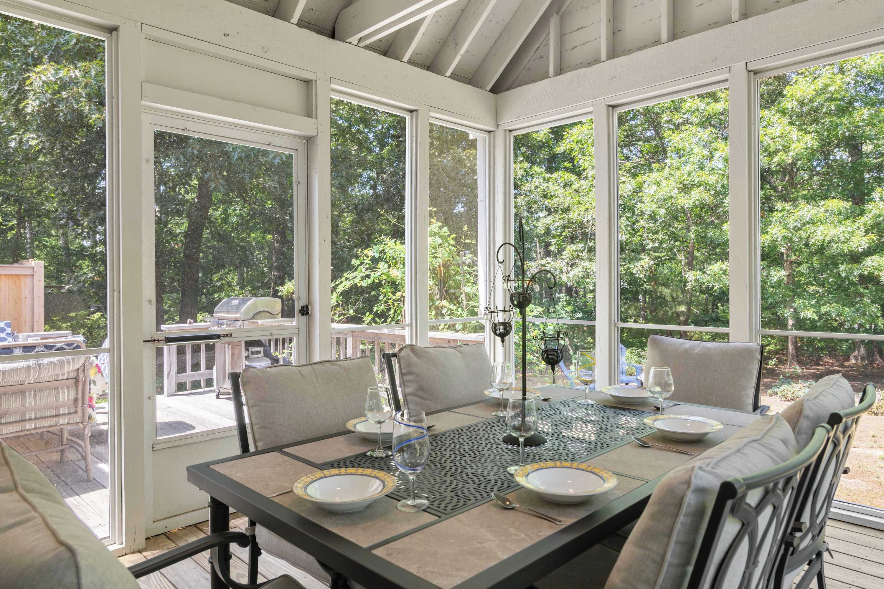 A conservatory with a glass table set for dining, surrounded by chairs and a view of the outdoors.