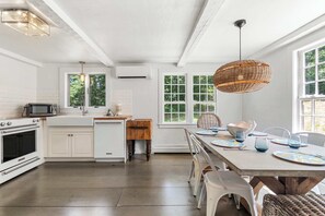 A modern kitchen with white cabinetry, a dining area with a wooden table, and large windows.