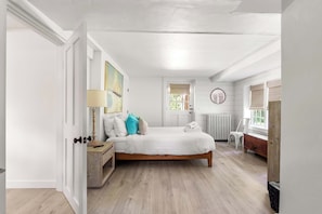 A bedroom with a bed, bedside table, lamp, and a painting.