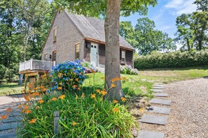 Ein Holzhaus mit einer Veranda, umgeben von einem Kiesweg und verschiedenen Blumen.