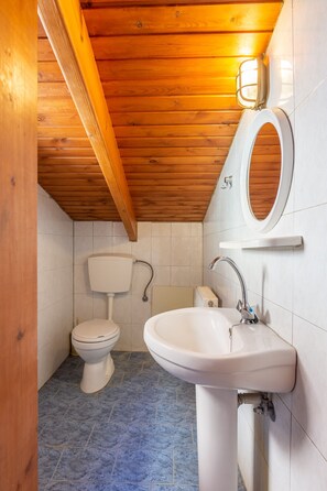 Ein kleines Badezimmer mit Holzboden, Toilette, Waschbecken und Spiegel.