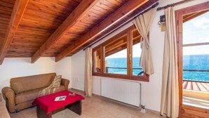 A room with a wooden ceiling, a sofa, a table with a red tablecloth, and a view of the sea through large windows. - Villa Maria Apt 2 (Ligres)