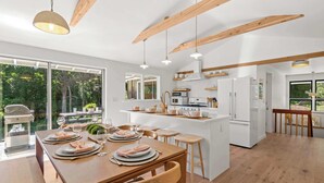 Una cocina moderna con vigas de madera, un comedor con mesa y sillas de madera, y vistas al exterior.