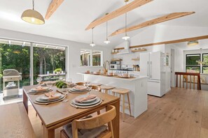 Eine moderne Küche mit Holzbalken, ein Essbereich mit Holztisch und -stühlen sowie ein Blick ins Freie.