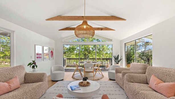 Una sala moderna con un ventanal grande, una lámpara colgante y un balcón con mobiliario exterior.