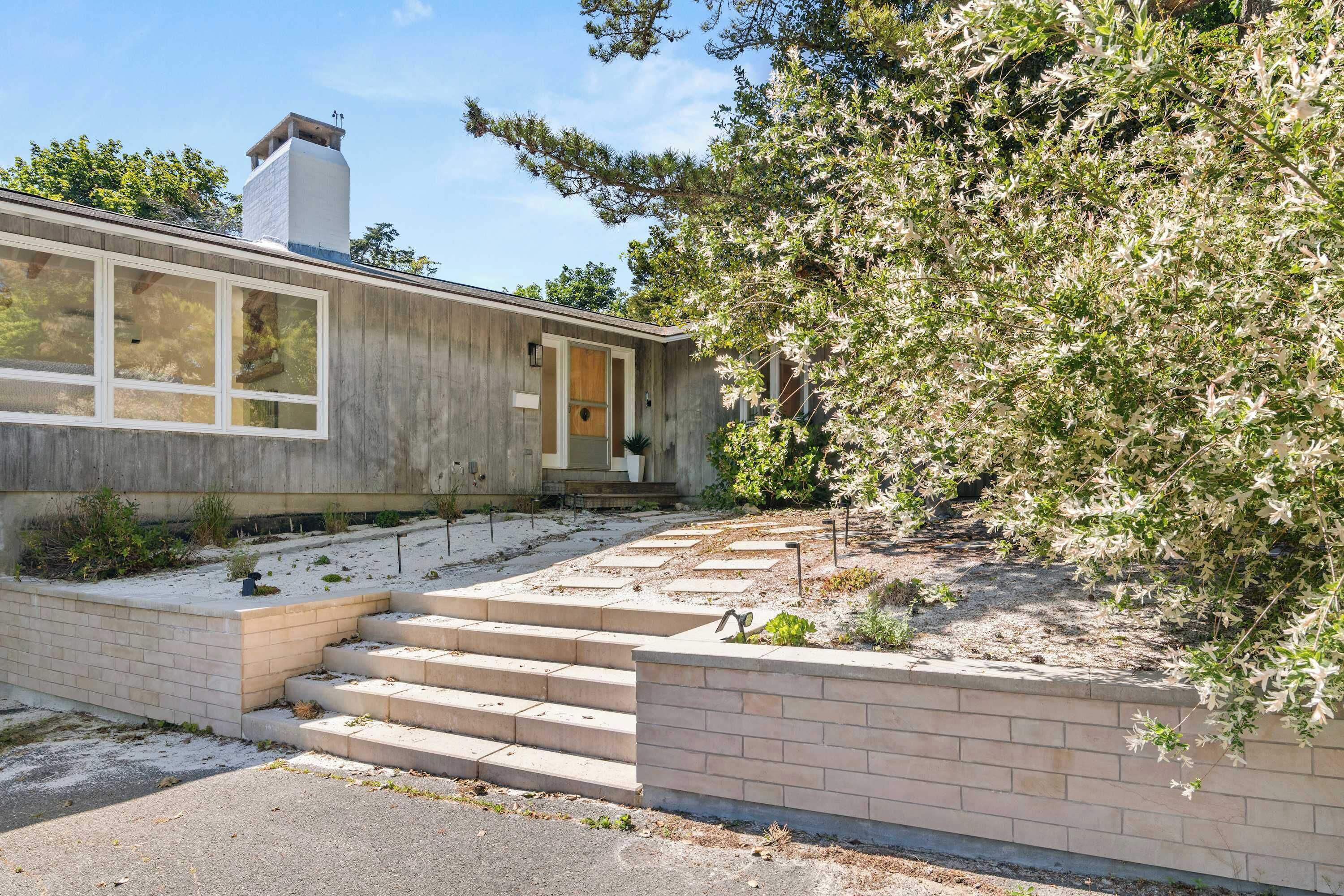 Een modern huis met een betonnen gevel, een schoorsteen en een stenen trap naar de voordeur.