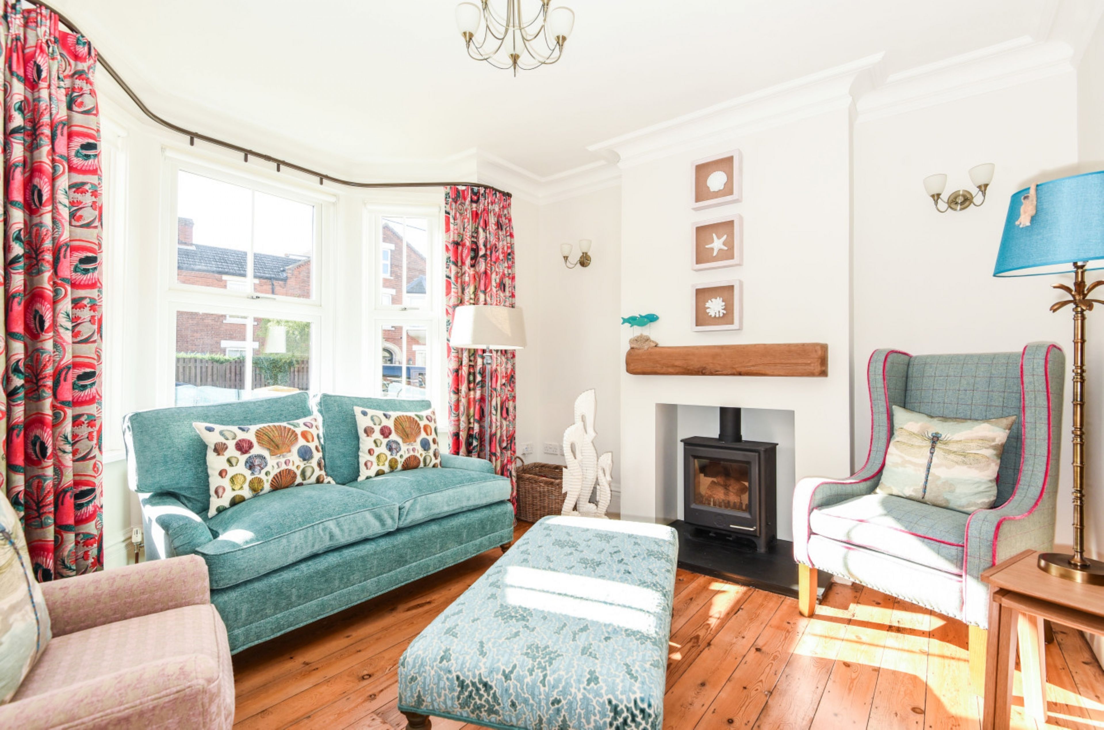 A cozy living room with a teal sofa, a patterned ottoman, a wooden chair, and a fireplace.