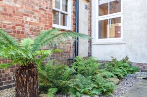 A brick building with a white window and a potted fern plant in the foreground. - Beach House - sleeps 5 guests  in 3 bedrooms (Hunstanton)