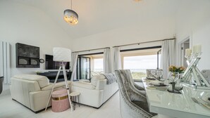 Una sala de estar moderna con un sofá, una mesa de comedor preparada para cuatro personas y un ventanal con cortinas.