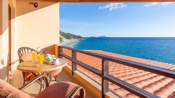 Un balcone con tavolo e sedie, vista sulla spiaggia e sul mare.