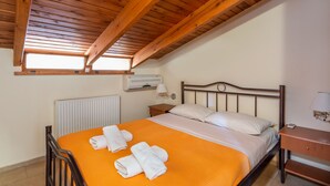 Una camera da letto con soffitto in legno, un letto con copriletto arancione, cuscini bianchi e un comodino con una lampada.