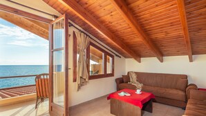 Una stanza con soffitto in legno, un divano, un tavolo con tovaglia rossa e vista mare attraverso una finestra.
