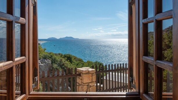 A view from a wooden-framed window overlooking a coastal landscape with a clear sky and distant mountains. - Villa Maria Studio 4 (Ligres)