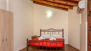 A bedroom with a wooden ceiling, a metal bed frame, a red bedspread, and a nightstand with a lamp. - Villa Maria Studio 4 (Ligres)