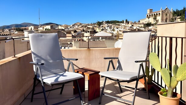 Een balkon met twee witte stoelen, een klein houten tafeltje en een cactus in een pot.