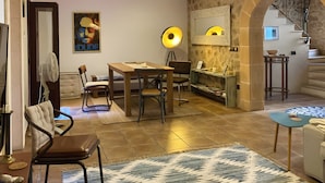 Een gezellige zithoek met een houten eettafel, stoelen, een vloerlamp en een trap naar een hoger gelegen verdieping.