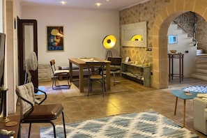 Una sala acogedora con una mesa de comedor de madera, sillas, una lámpara de pie y una escalera que sube a un nivel superior.