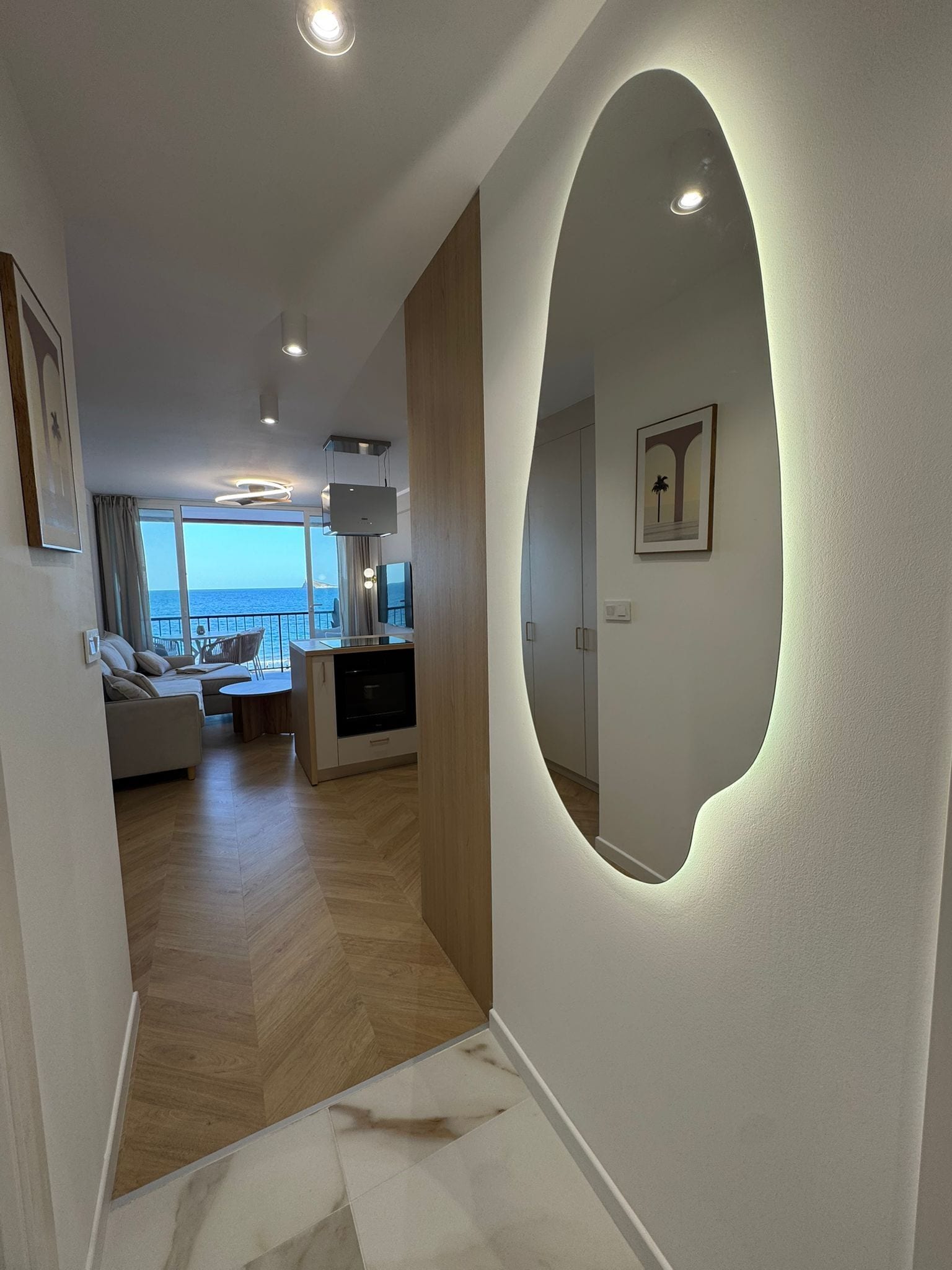 Una sala de estar moderna con un espejo grande, un sofá, un comedor y vistas al mar.