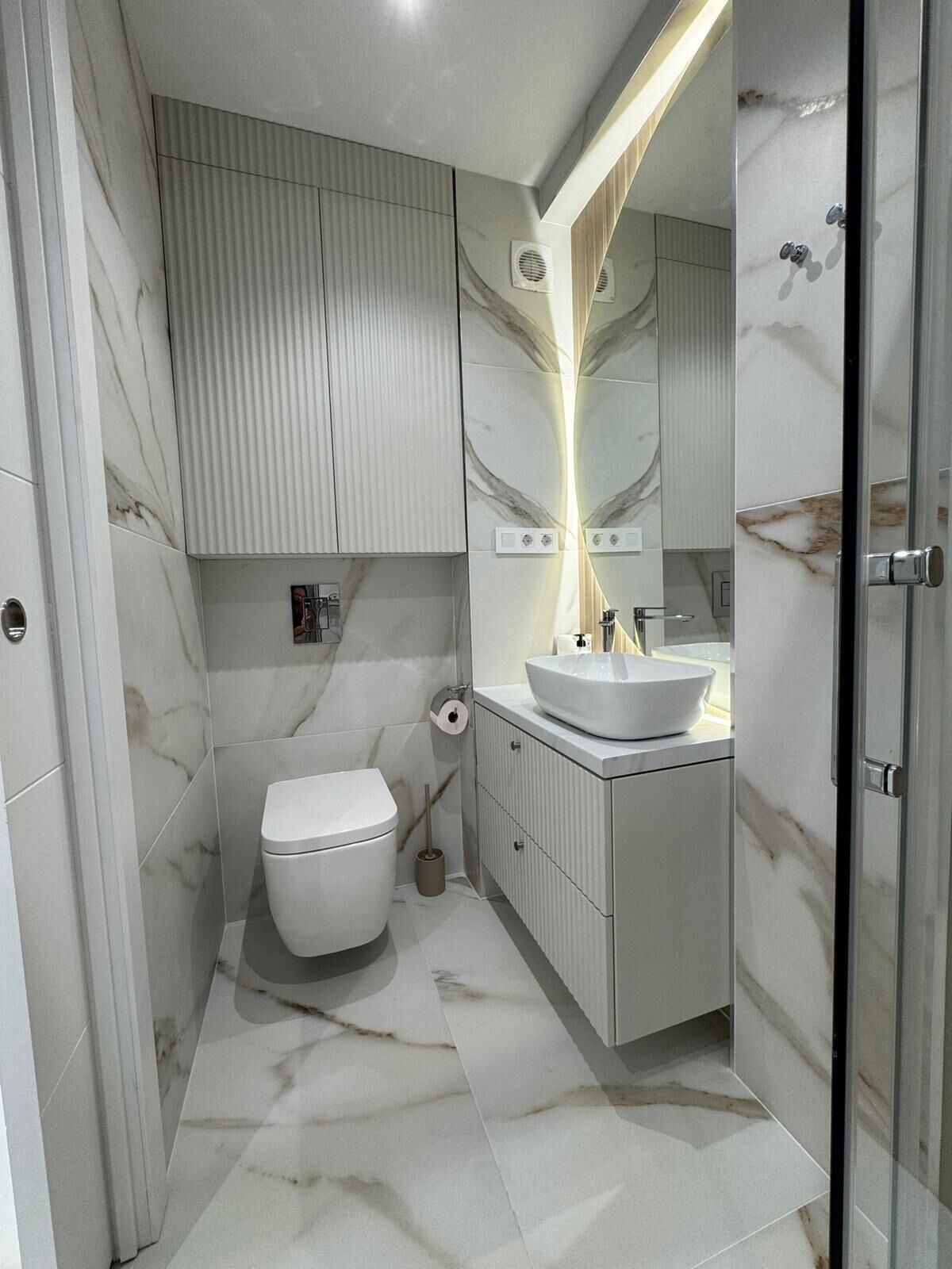 A modern bathroom with a white toilet, a vanity with a sink, and a mirror.
