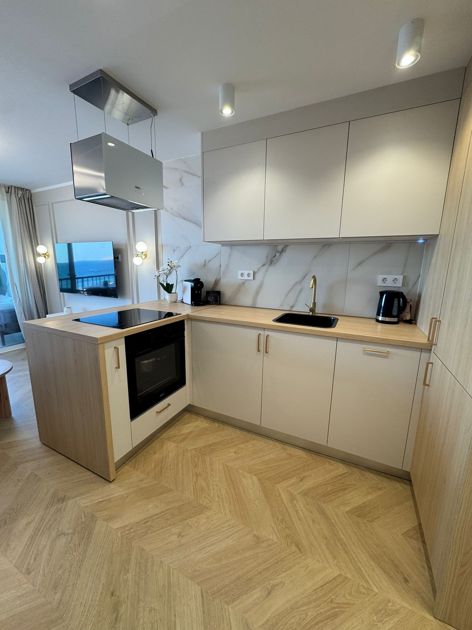 Una cocina moderna con horno empotrado, pileta y estufa. Hay una ventana con vista al mar y el piso es de madera.