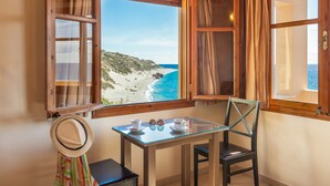 Una habitación con vista a la playa, una mesa con tazas y un sombrero, y una silla.