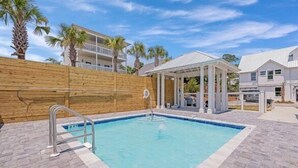 Piscina com cerca de madeira, área de estar coberta e vista para edifícios residenciais.
