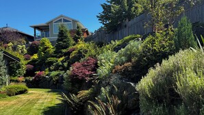 Ein gepflegter Garten mit verschiedenen Pflanzen und einer Rasenfläche, begrenzt von einem Holzzaun und einem Haus im Hintergrund.