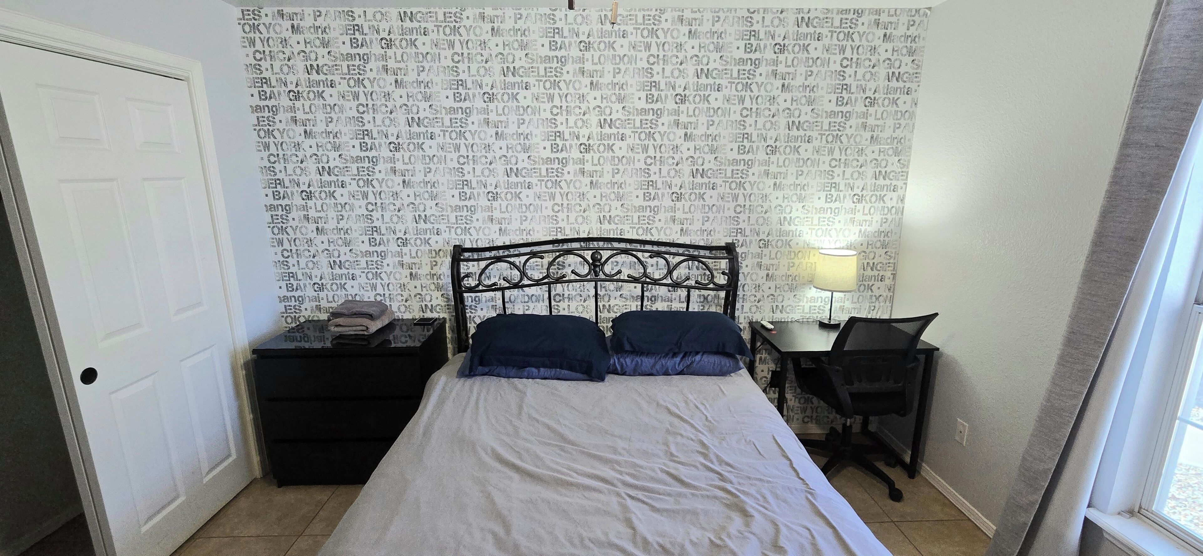 Een slaapkamer met een bed, nachtkastje, bureau en lamp.