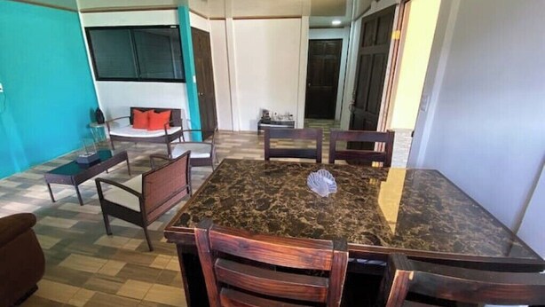 Un espace repas avec une table en marbre et des chaises en bois, un canapé et, au fond, un coin cuisine.