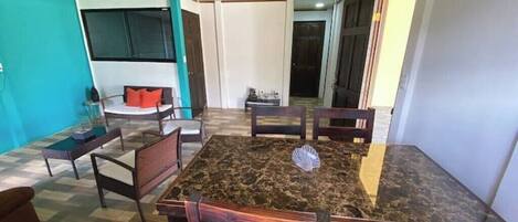 Un comedor con una mesa de mármol y sillas de madera, un sofá y una zona de cocina al fondo.