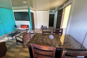A dining area with a marble table and wooden chairs, a sofa, and a kitchen area in the background.