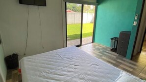 Une chambre à coucher comprenant un lit, un téléviseur fixé au mur, une porte-fenêtre coulissante donnant sur un patio, et un petit bureau avec un classeur.