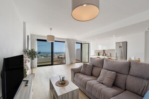 Ein modernes Wohnzimmer mit Flachbildfernseher, einer Couch, einem Couchtisch und Blick auf die Stadt.