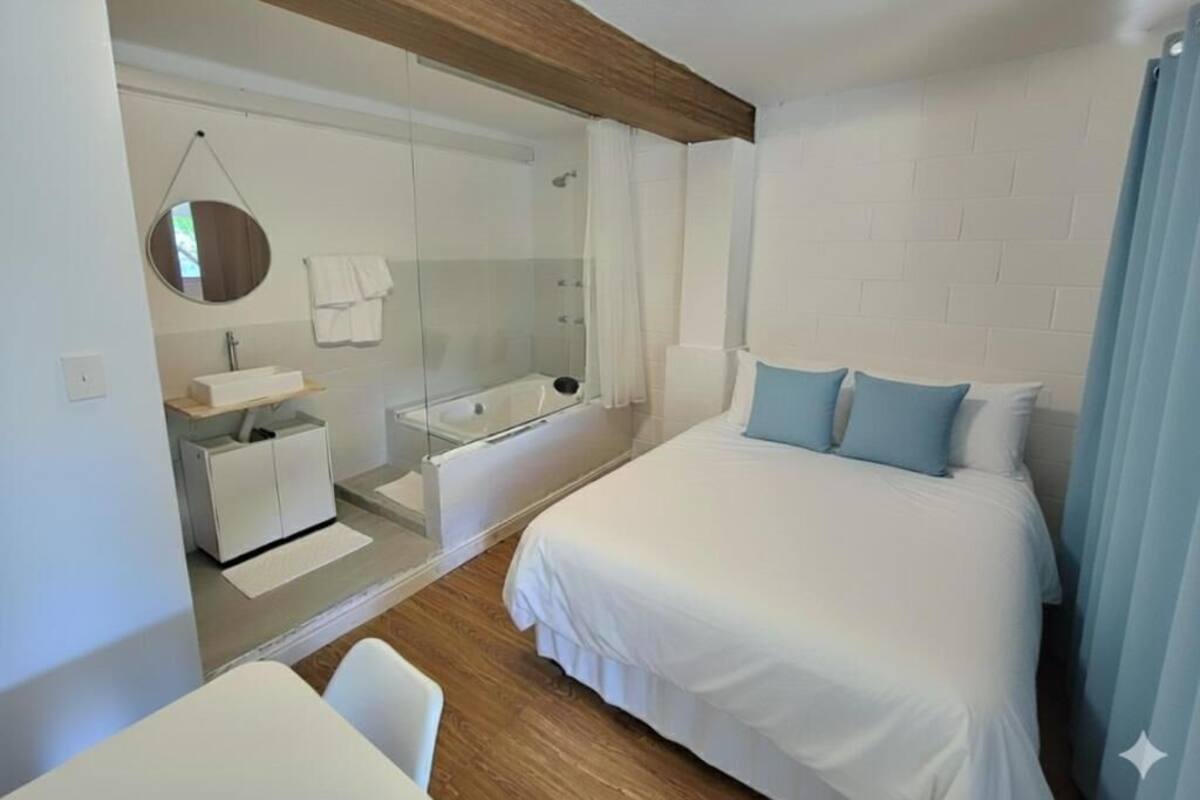 A modern bedroom with a bed, a shower, and a small desk area.