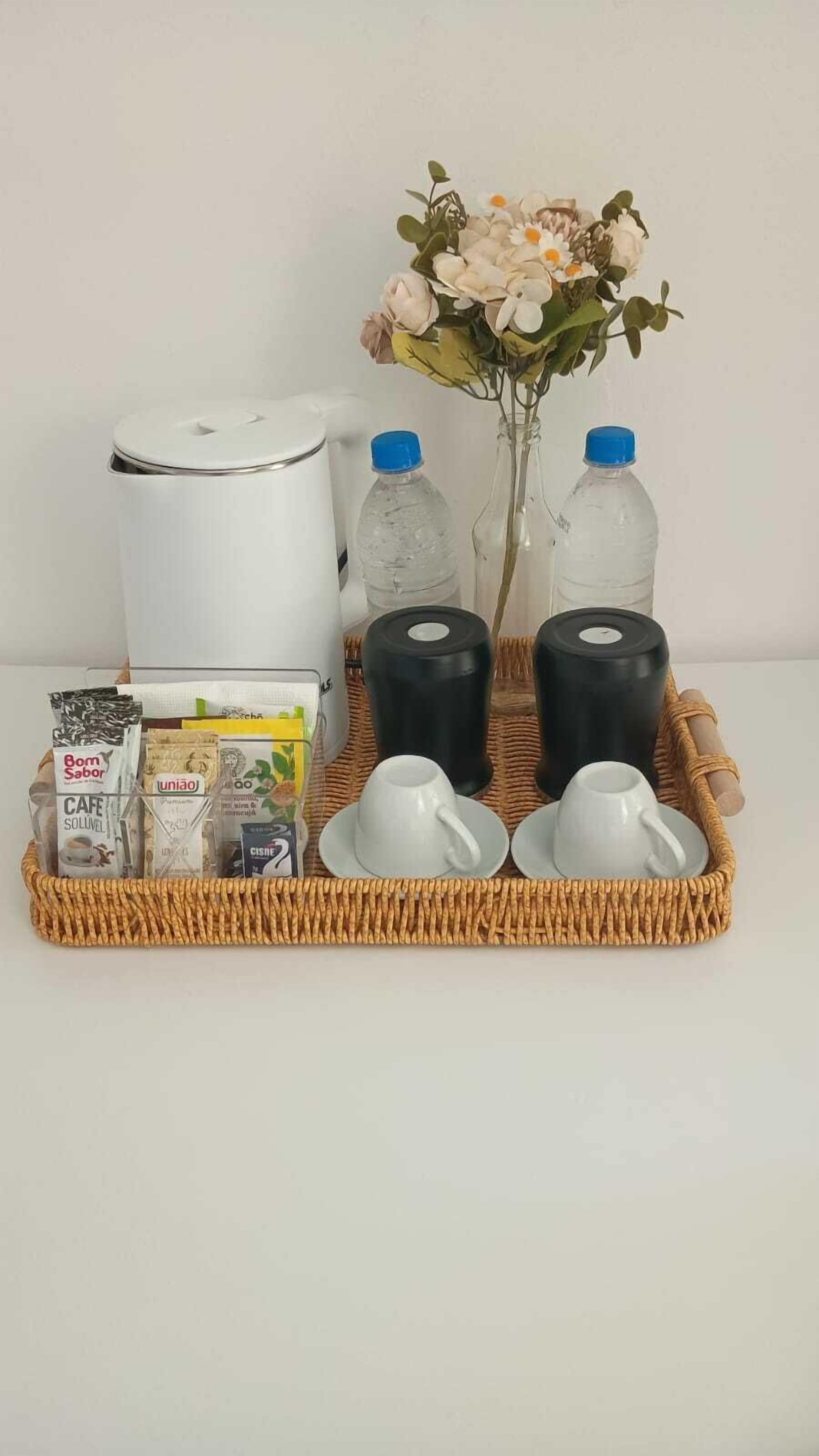 Un plateau avec une cafetière, deux bouteilles, un vase de fleurs et un panier contenant des articles de toilette.