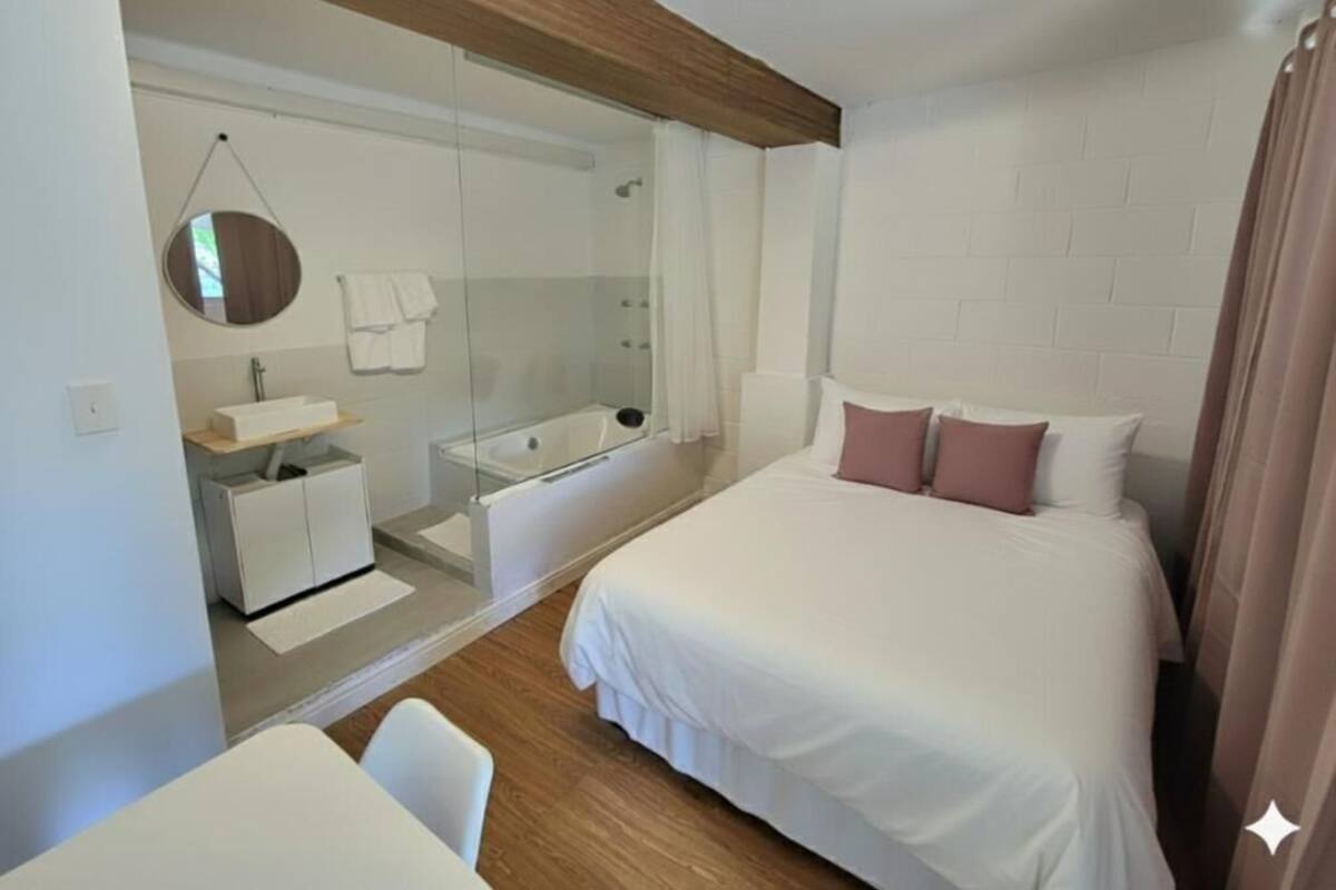 A modern hotel room with a large bed, a separate bathroom with a glass shower, and a small seating area.