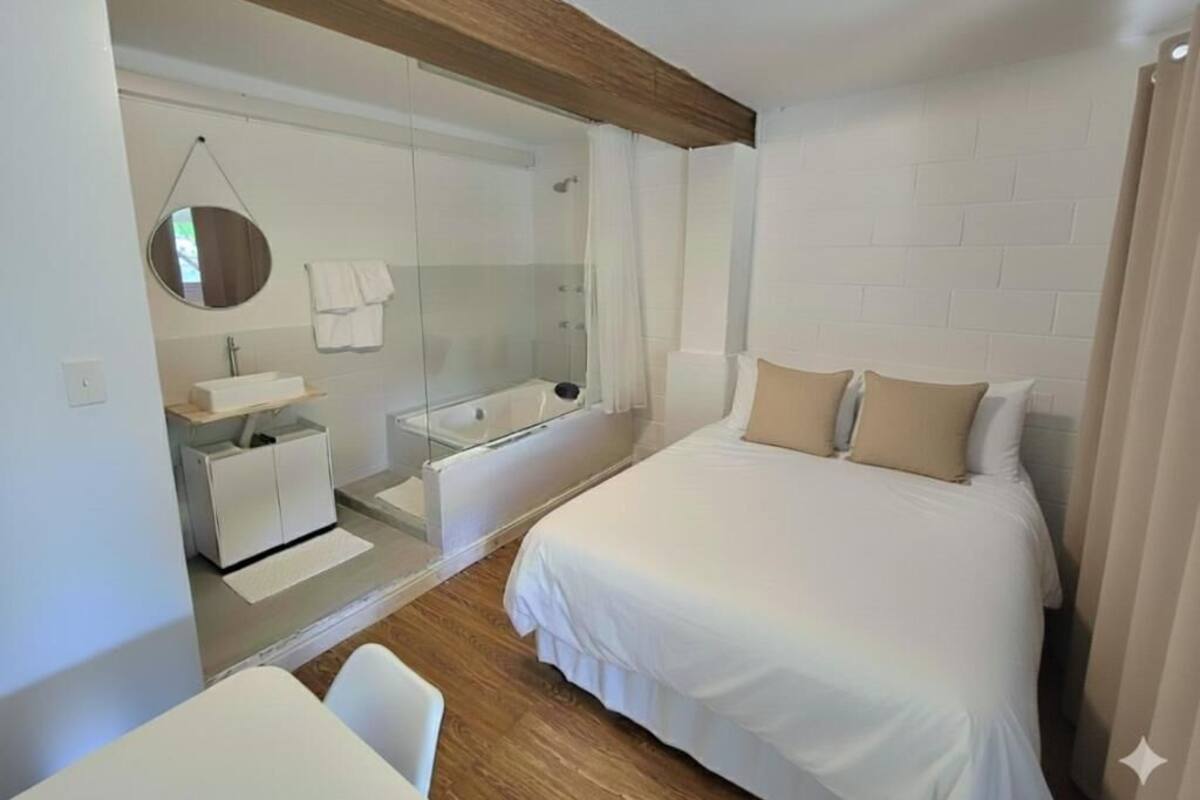 A modern hotel room with a large bed, a separate bathroom with a glass shower, a small desk, and a round mirror.