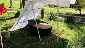 Un espacio al aire libre con toldo blanco, una mesa redonda de mimbre negro y un césped con árboles.