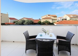 Ein Balkon mit zwei Korbstühlen und einem Tisch, mit Blick auf eine Wohngegend mit Häusern und Grünflächen.