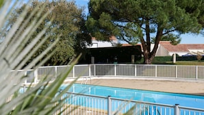 Una piscina con recinzione bianca, circondata da alberi e un edificio con tetto rosso.