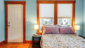 A bedroom with a wooden door, two windows with blinds, a bed with floral bedding, and two bedside lamps. - 9 Mi to Wachusett Mtn! Family Base w/ Porch (Fitchburg)